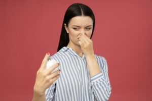 Dissatisfied woman with perfume bottle in hand on pink background