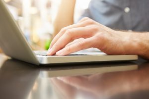 male hand typing on laptop at outside cafe