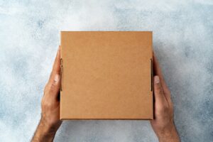 Parcel cardboard box in a man hands on a gray table background